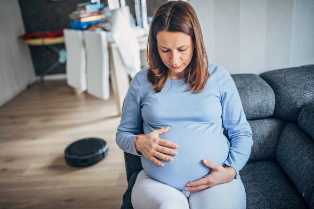 istock Woman sitting on sofa while robot vacuum cleaner is cleaning the floor 1194874334