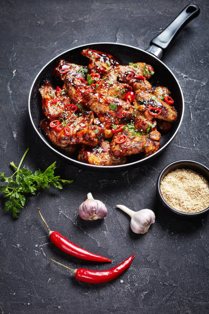 teriyaki chicken wings sprinkled with sesame seeds, chili pepper pieces and parsley crispy teriyaki chicken wings sprinkled with sesame seeds, chili pepper pieces and parsley in a skillet on a concrete table, vertical view from above sticky sesame chicken sauces stock pictures, royalty-free photos & images