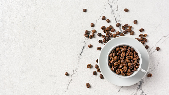 Top view of coffee beans in white cup for breakfast on marble background with copy space