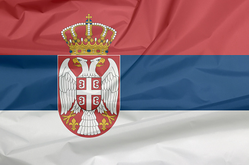 Fabric flag of Serbia. Crease of Serbian flag background, a horizontal tricolor of red blue and white; charged with the lesser Coat of arms left of center.