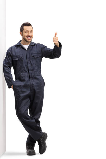 jeune travailleur masculin dans un uniforme se penchant sur le mur et affichant des pouces vers le haut - manual worker full length isolated on white standing photos et images de collection