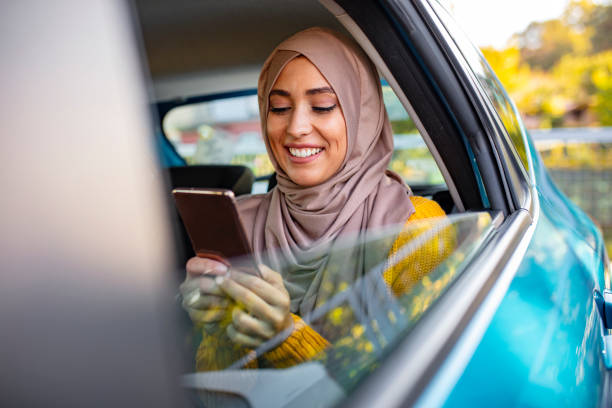 Muslim business woman in car. Muslim business woman in car. Writing a message on her mobile phone. Positive pensive Islamic woman in hijab sitting on backseat of taxi and drinking coffee while using gadget arabian girl stock pictures, royalty-free photos & images