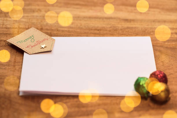 Christmas Background - flat lay image of a white blank card with decorative ornaments, a tag and yellow lights bokeh on wooden table with copy space.