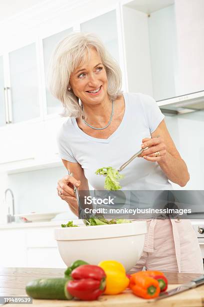 Mujer Senior Ensalada De Preparación En La Cocina Foto de stock y más banco de imágenes de 60-69 años - 60-69 años, Adulto, Adulto maduro