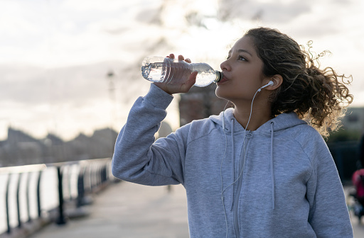 Portrait of a young woman drinking water while running outdoors in London