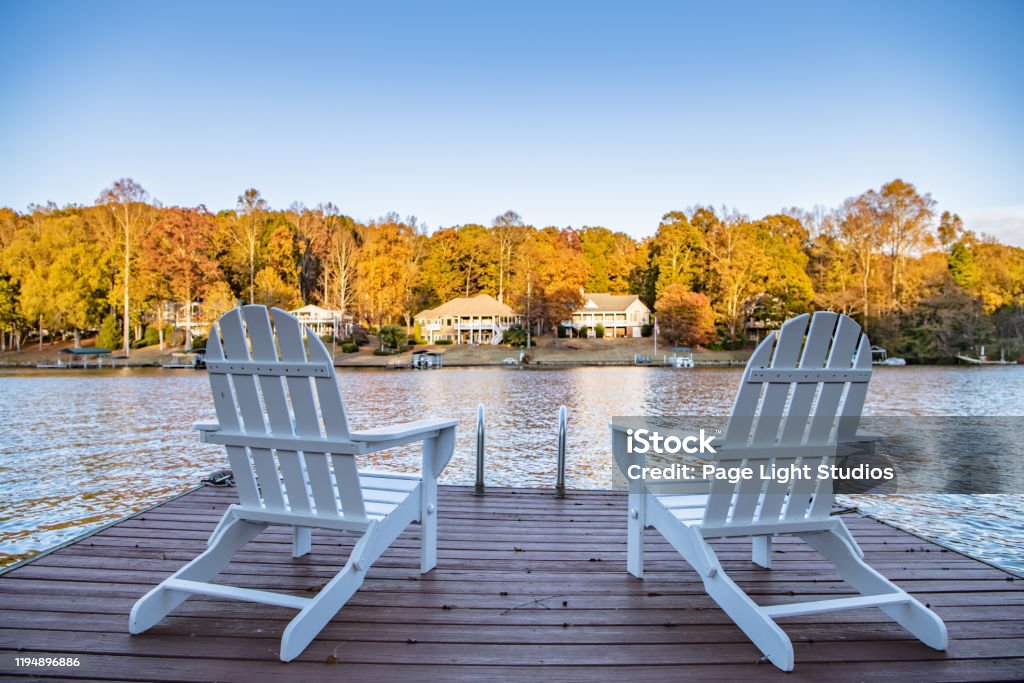 Two Adirondack style chairs on a dock Adirondack style chairs on a dock, overlooking a beautiful, quiet, lake. Concept of a relaxing vacation in a remote area. Small Town America Stock Photo