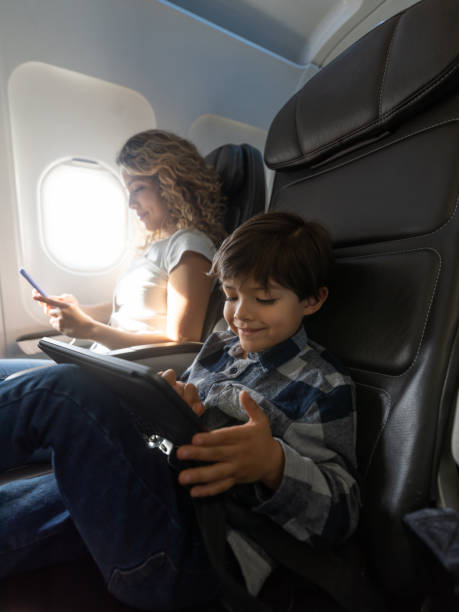 istock Happy little boy playing with tablet during a flight while mom is chatting on smartphone 1194896946