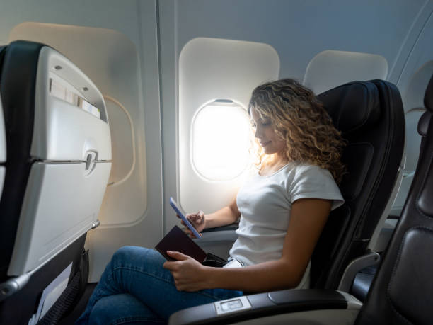 mujer latinoamericana sentada junto al asiento de la ventana en el avión enviando mensajes de texto en el teléfono inteligente - silla al lado de la ventana fotografías e imágenes de stock