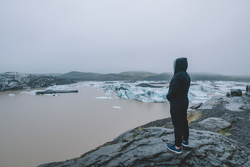 an asiian chinese male tourist standing in front of glacier viewing from top at iceland