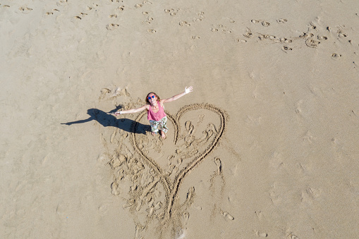 Young woman standing in drawn heart on sand beach in Hawaii, USA