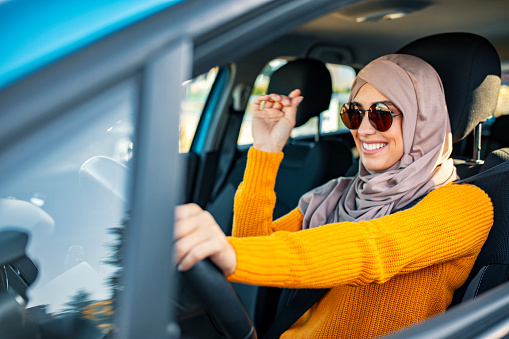Beautiful  Muslim woman driving a car wearing hijab. Emirati woman driving a car in Dubai at sunset. Portrait of a Middle Eastern woman driving a car, she is wearing a modern beige Abaya.