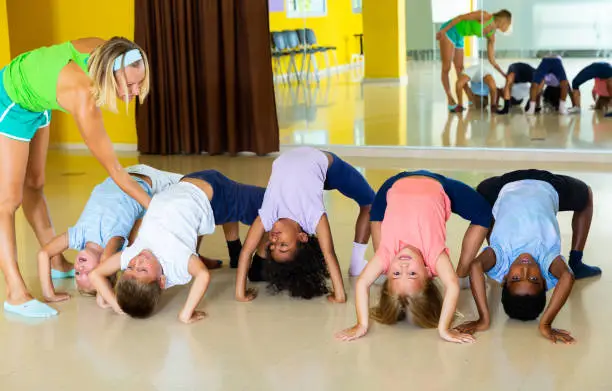 Photo of Children with trainer stretching in dance classroom