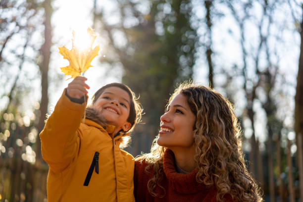 彼女の息子が公園で晴れた秋の日に保持している葉を見て美しい母親 - autumn women smiling leaf ストックフォトと画像