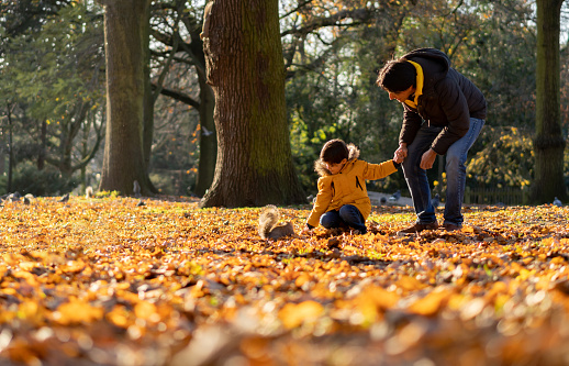 Loving father holding his sons hand while he is feeding a squirrel at the park on an autumn day - Lifestyles