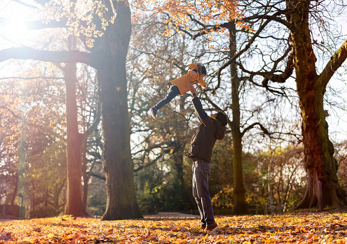 Happy father throwing his cute son to the air having fun at the park on an autumn day - Lifestyles