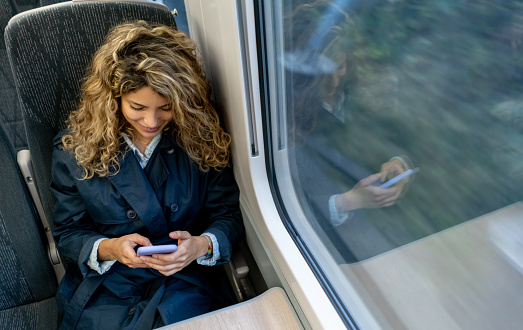 Beautiful young woman traveling by train texting on smartphone smiling - Lifestyles