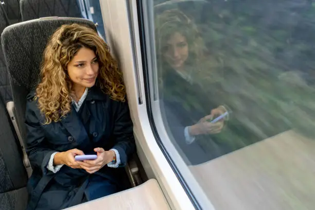 Photo of Beautiful woman traveling by train looking at the view while texting on smartphone