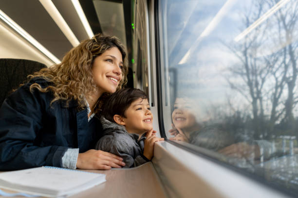 Happy single mother and son looking at the window view both smiling while traveling by train Happy single mother and son looking at the window view both smiling while traveling by train - Lifestyles passenger train stock pictures, royalty-free photos & images