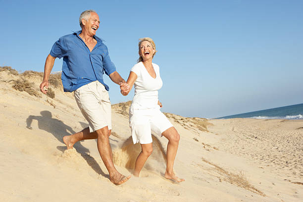 Senior Couple Enjoying Beach Holiday Running Down Sand Dune
