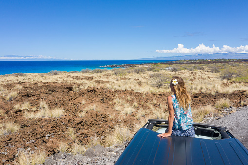 Young woman sitting on vehicle looking at seascape in Hawaii, USA