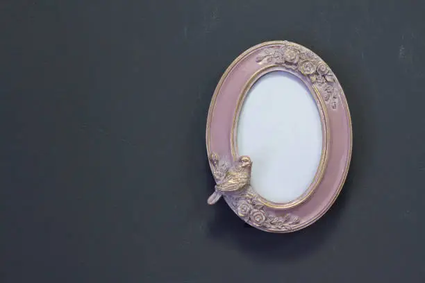 Photo of Empty pink-gold vintage oval frame in Victorian style on a gray wall, background or concept