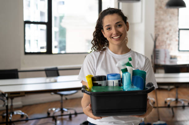 verticale de beau nettoyeur féminin retenant un seau avec des approvisionnements de nettoyage à un bureau souriant à l'appareil-photo - agent de ménage photos et images de collection