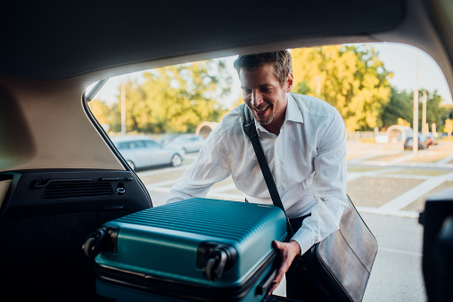 Businessman packing a suitcase in the car trunk and preparing for the business travel.