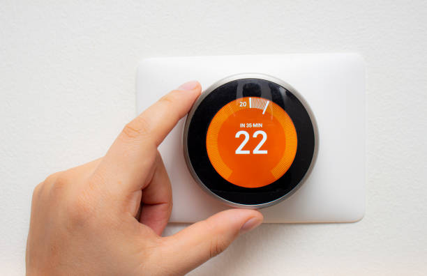 istock Smart Thermostat with a person warming up the room temperature with a soft shadow 1194920569