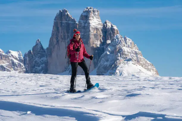 active senior woman snowshoeing under the famous Three Peaks, from Prato Piazzo up to the Monte Specie in the three peaks Dolomites area near village of Innichen, South Tyrol, Italy