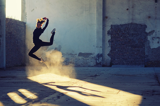 Silhouette of ballerina dancing in an abandoned building on a sunny day.