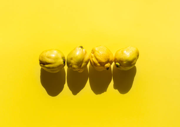 Tasty fresh quinces on a yellow background in harsh light. Above view of autumn fruits. Four pieces of quince fruit. Flat lay of healthy fall snacks.