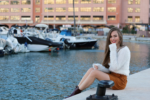 Woman Fashion Model In White Fluffy Knitted Pullover And Brown Miniskirt In The Monaco Harbor