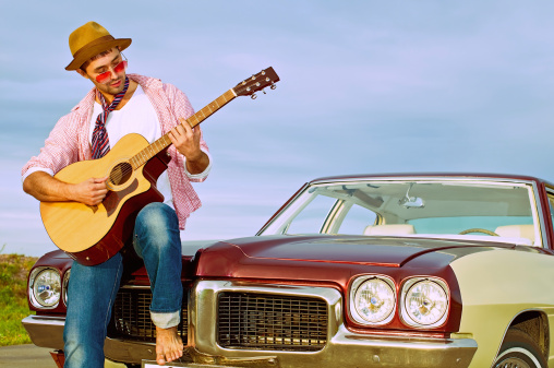 Bearded man playing guitar outdoors near retro carBearded man behind the wheel of a retro car