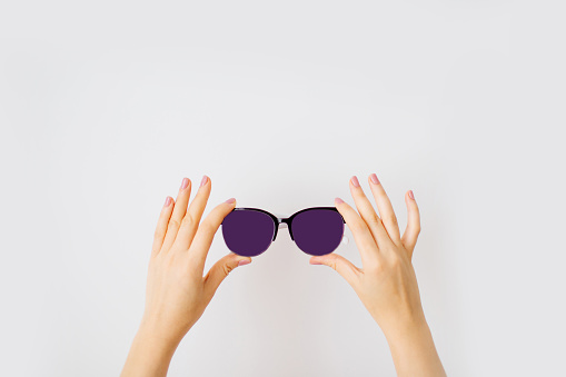 Female hands holding stylish sunglasses with dark purple lens isolated on white background.