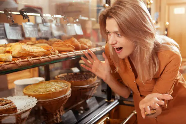 Mature woman looking overwhelmed, choosing desserts from the display at bakery store