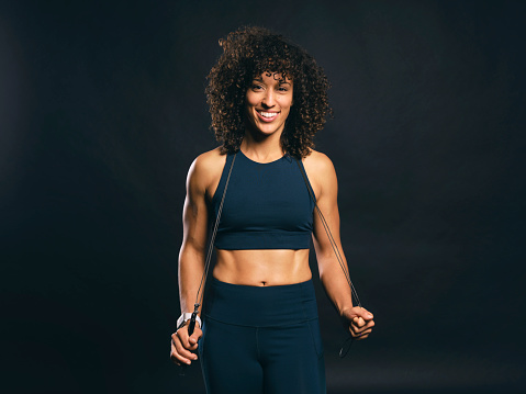 A physically fit woman standing with a jump rope against a black background.