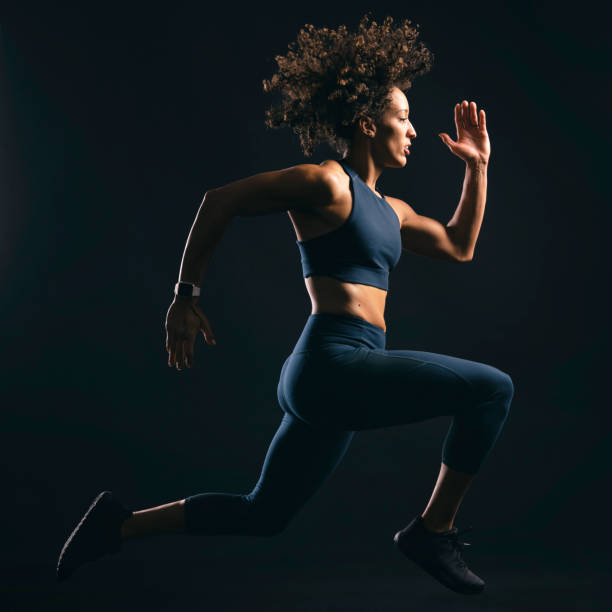 Fit Woman Jumping A physically fit woman jumping in a running pose against a black background. fitness tracker photos stock pictures, royalty-free photos & images