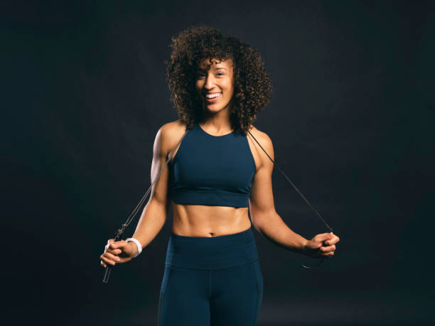 A physically fit woman standing with a jump rope against a black background.