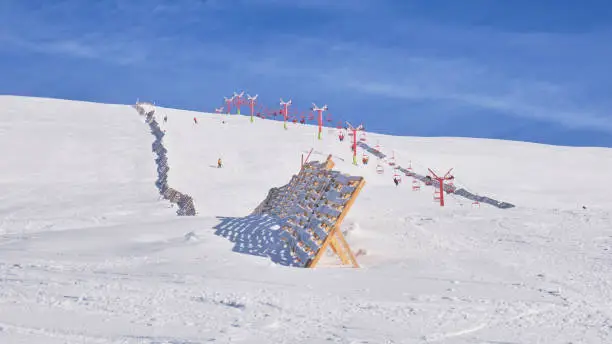 Photo of Sinaia ski domain. View of a medium difficulty slope in Valea Dorului, a wooden protection fence, and an old, red, chairlift. Popular Winter resort in Bucegi mountains, Romania.