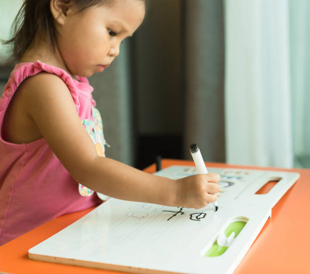 ein kleines mädchen lernt, wie man alphabete zu hause schreibt. kindererziehung. - reading and writing classroom alphabet learning stock-fotos und bilder