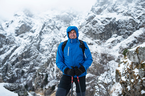 Front view portrait of adult man hiker in mountain, winter season, cheerful portrait in front of snow mountain range.