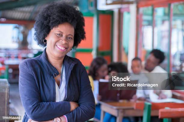 An Afro Grandmother Smiling At The Camera While Her Family Orders On The Menu In The Background Of The Photo Stock Photo - Download Image Now