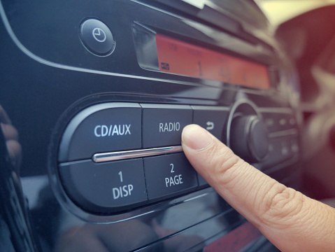 Close up image of driver's hand press button on car radio, listening music during trip concept