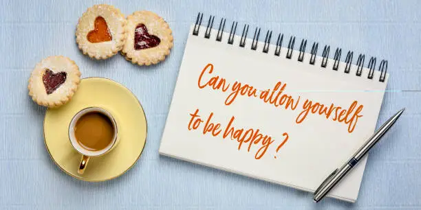 Can you allow yourself to be happy? Inspirational question in a sketchbook with a cup of coffee and heart biscuits. Happiness and positivity concept.