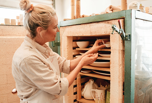 Shot of a artisan placing earthenware in her kiln