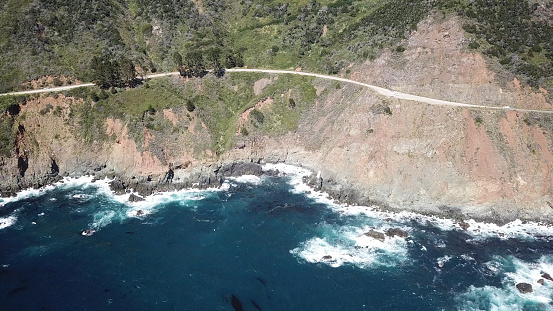 Drone aerial photo of the California coastline and McWay Falls by Big Sur. Big Sur is a rugged stretch of California’s central coast between Carmel and San Simeon. Bordered to the east by the Santa Lucia Mountains and the west by the Pacific Ocean, it’s traversed by narrow, 2-lane State Route 1, known for winding turns, seaside cliffs and views of the often-misty coastline. The sparsely populated region has numerous state parks for hiking, camping and beachcombing.
