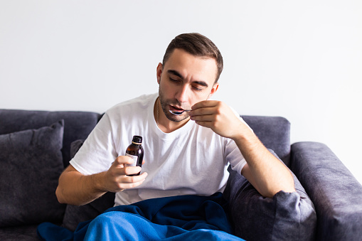 Enfermo hombre negro dejando caer la píldora de aspirina en el vaso de agua, sentado en el sofá en casa, espacio libre photo