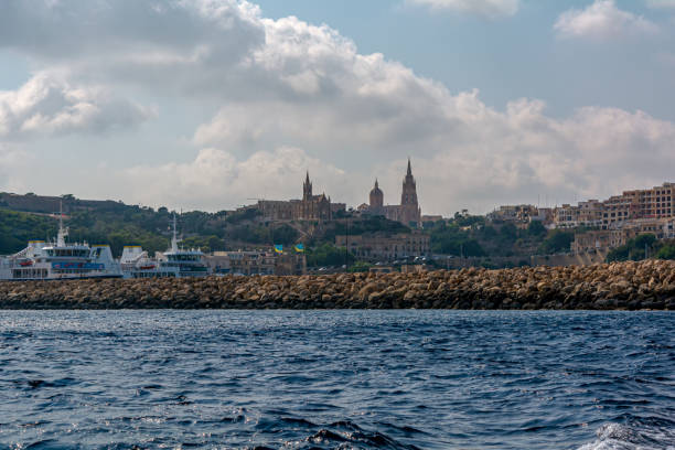 Gozo classic landscape with breakwater and ships in the sea Mgarr, Gozo, Malta - September 3, 2019: Gozo classic landscape with breakwater and ships in the sea, and Lourdes Chapel and Ghajnsielem Church on the hill in the distance. mgarr malta island gozo cityscape with harbor stock pictures, royalty-free photos & images