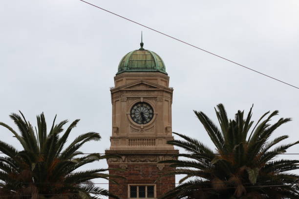 stara miedziana wieża zegarowa na tle zachmurzonego białego nieba otoczonego tropikalnymi palmami wzdłuż nadmorskiej promenady w melbourne, coastal victoria, australia - melbourne australia clock tower clock zdjęcia i obrazy z banku zdjęć