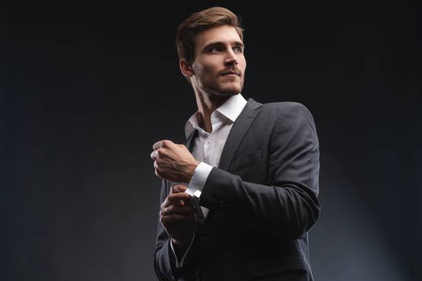 Perfect to the last detail. Handsome young businessman adjusting his sleeves while standing against gray background. Perfect to the last detail. Handsome young businessman adjusting his sleeves while standing against gray background metrosexual stock pictures, royalty-free photos & images